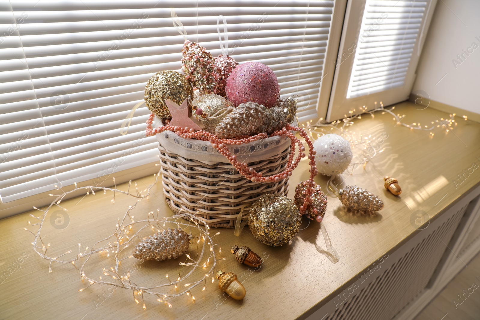 Photo of Basket with beautiful Christmas tree baubles and fairy lights on window sill indoors