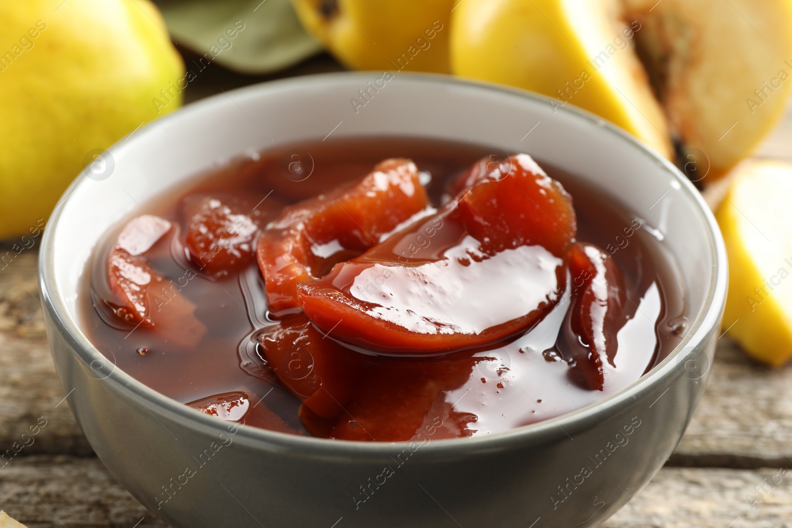 Photo of Tasty homemade quince jam in bowl on wooden table, closeup