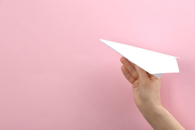 Photo of Woman holding paper plane on pink background, closeup. Space for text