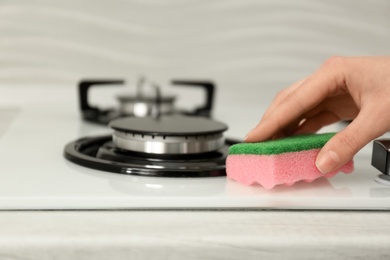 Photo of Woman cleaning gas stove with sponge, closeup