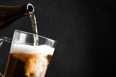 Pouring cold tasty beer from bottle into glass mug on black background, closeup. Space for text