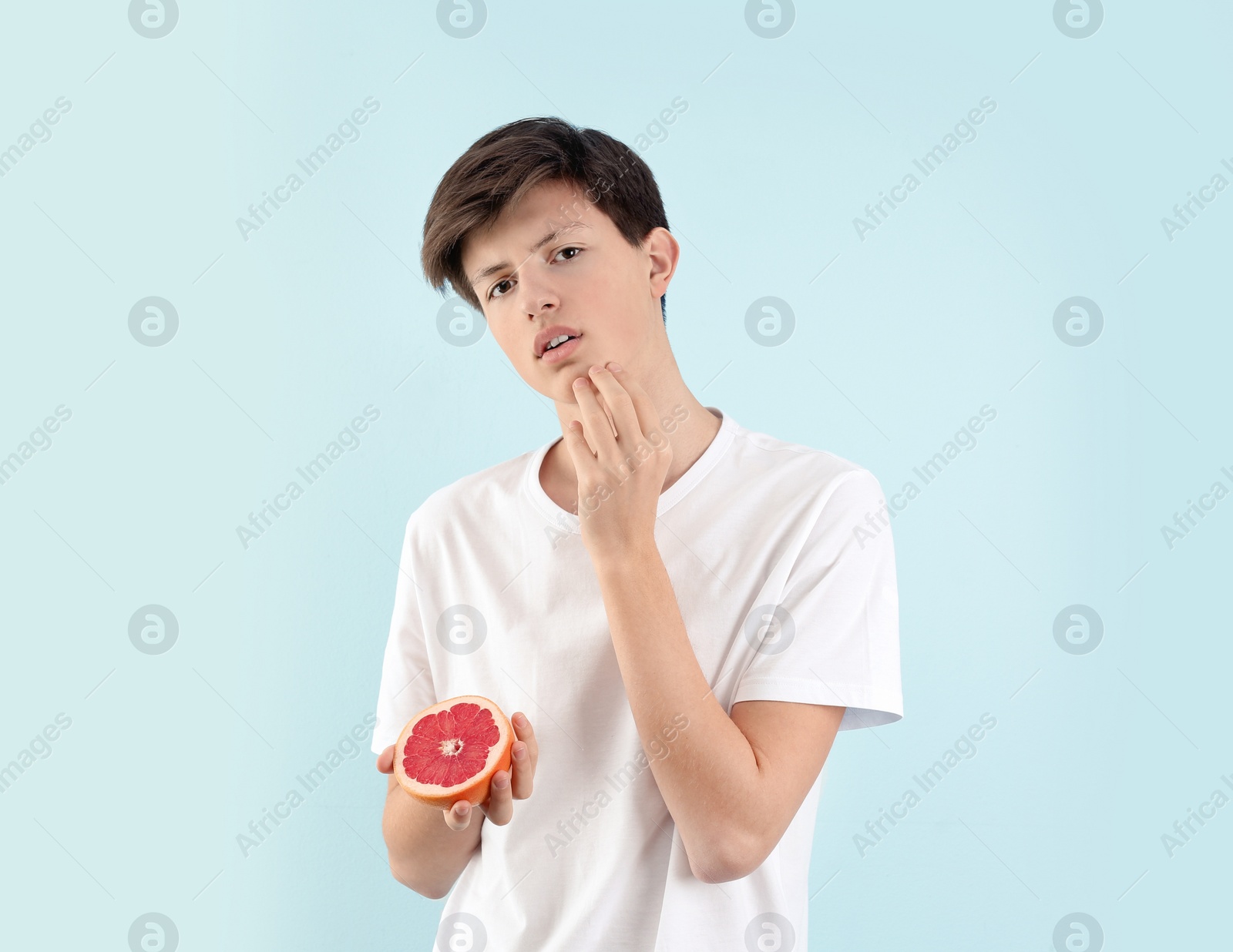 Photo of Teenage boy with acne problem holding grapefruit on light background. Skin allergy