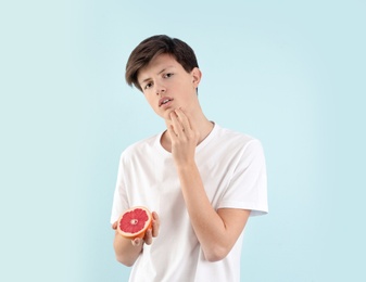 Teenage boy with acne problem holding grapefruit on light background. Skin allergy