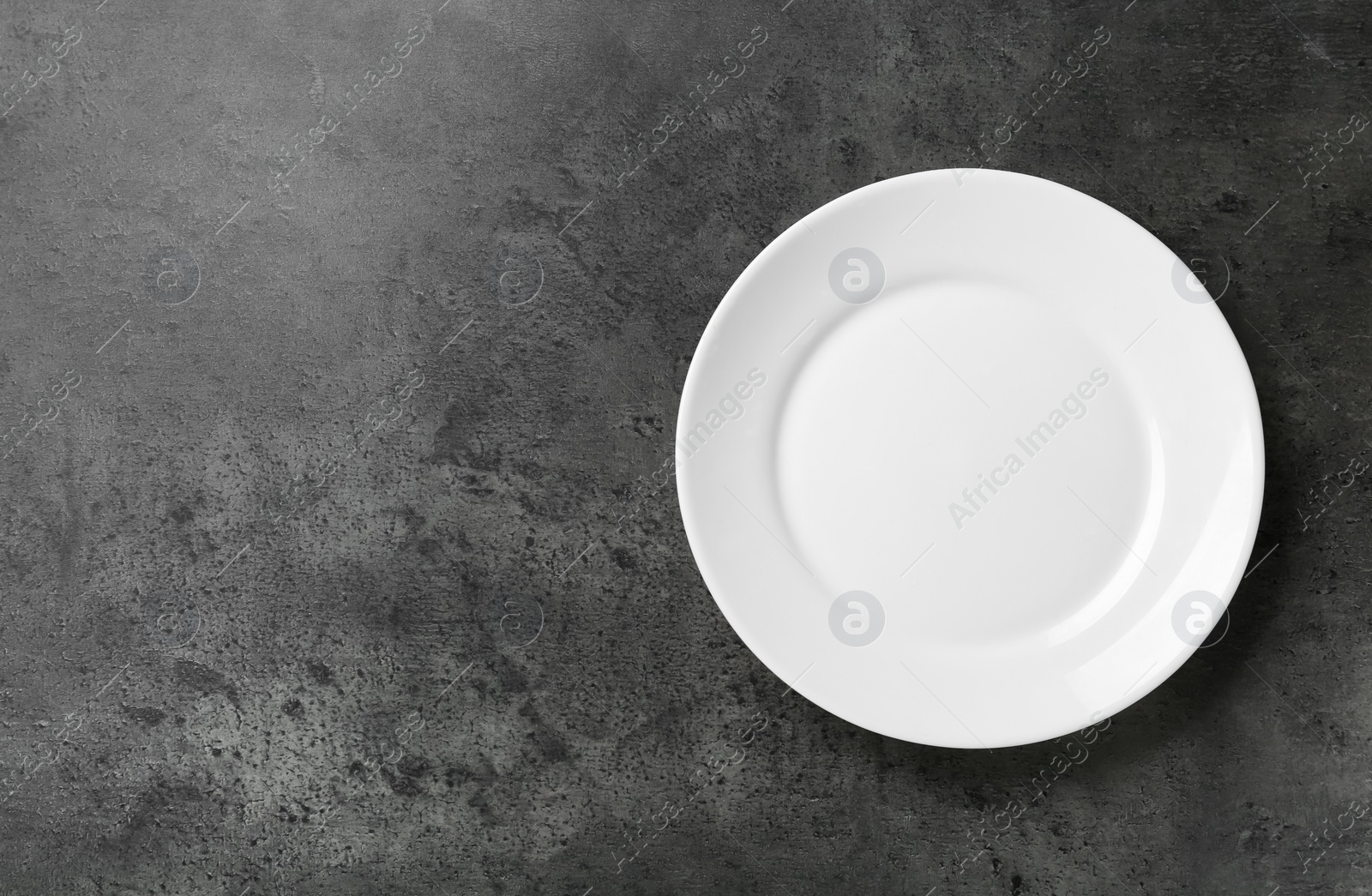 Photo of Clean white plate on grey table, top view. Space for text