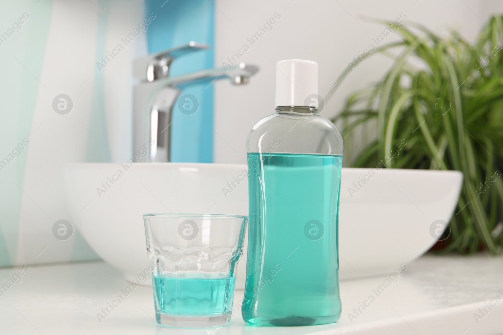 Photo of Bottle of mouthwash and glass on white table in bathroom