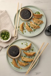 Photo of Delicious gyoza (asian dumplings) with soy sauce, green onions and chopsticks on white table, flat lay