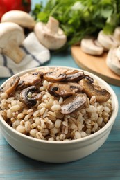 Delicious pearl barley with mushrooms in bowl on light blue wooden table, closeup