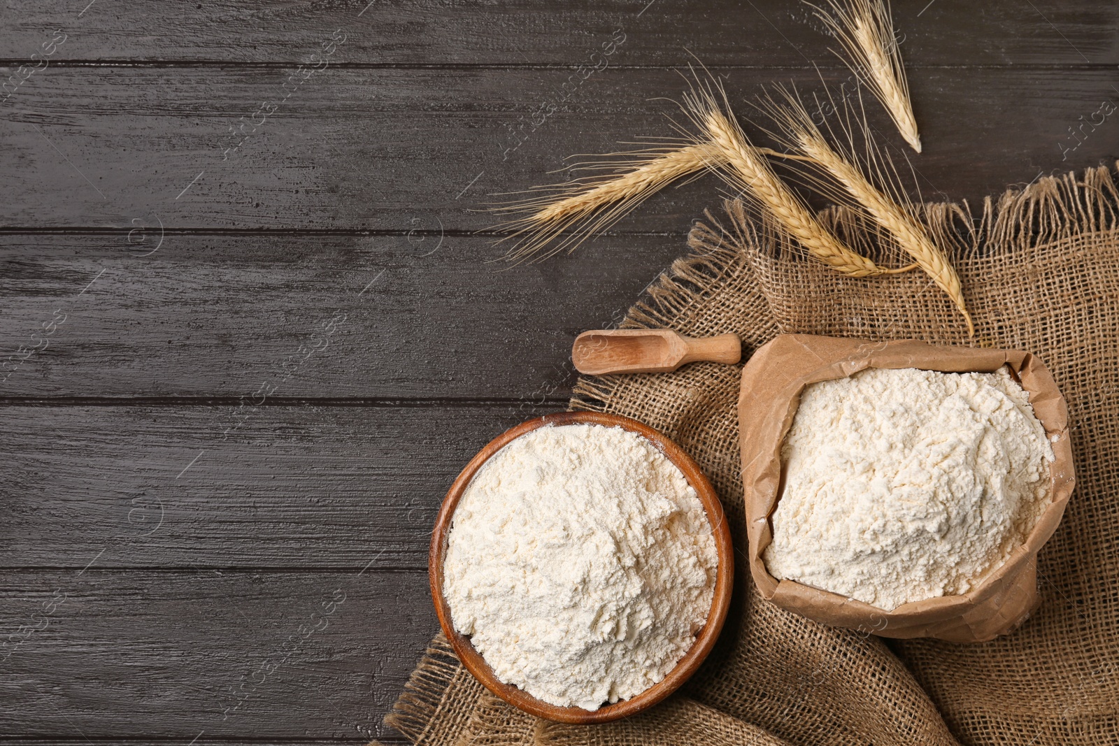 Photo of Bowl and paper bag with flour on wooden background