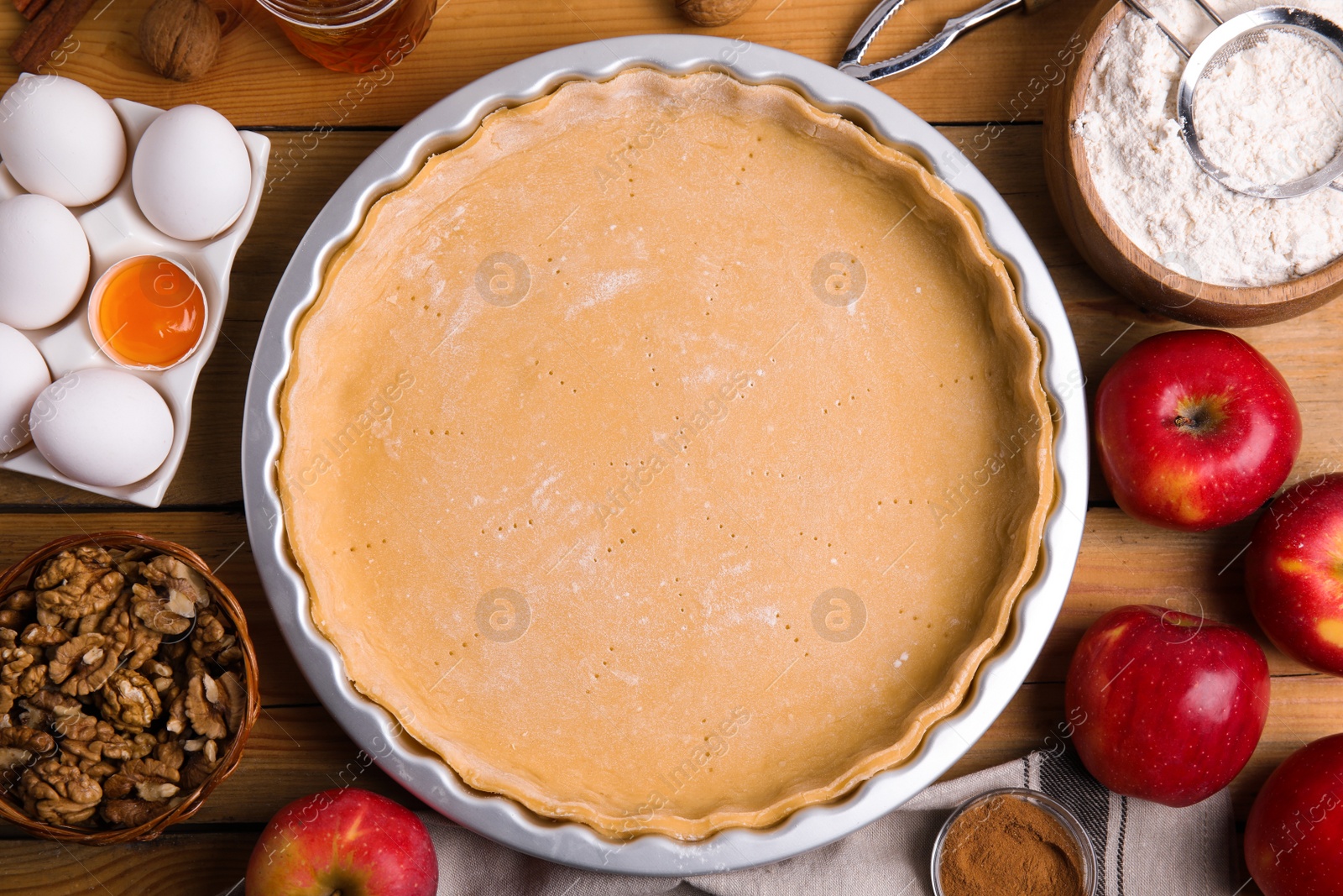 Photo of Raw dough and ingredients for traditional English apple pie on wooden table, flat lay