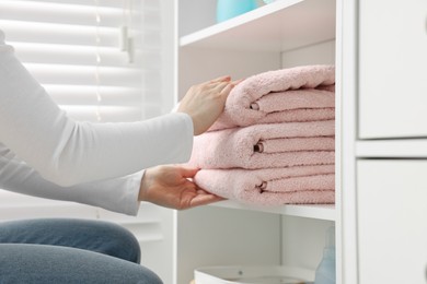 Photo of Woman stacking clean towels on shelf indoors, closeup