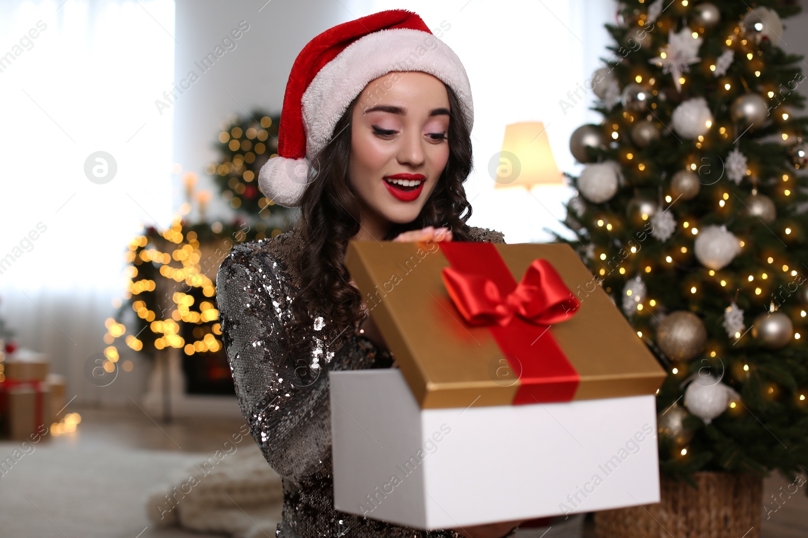 Photo of Beautiful woman in Santa hat opening Christmas gift at home