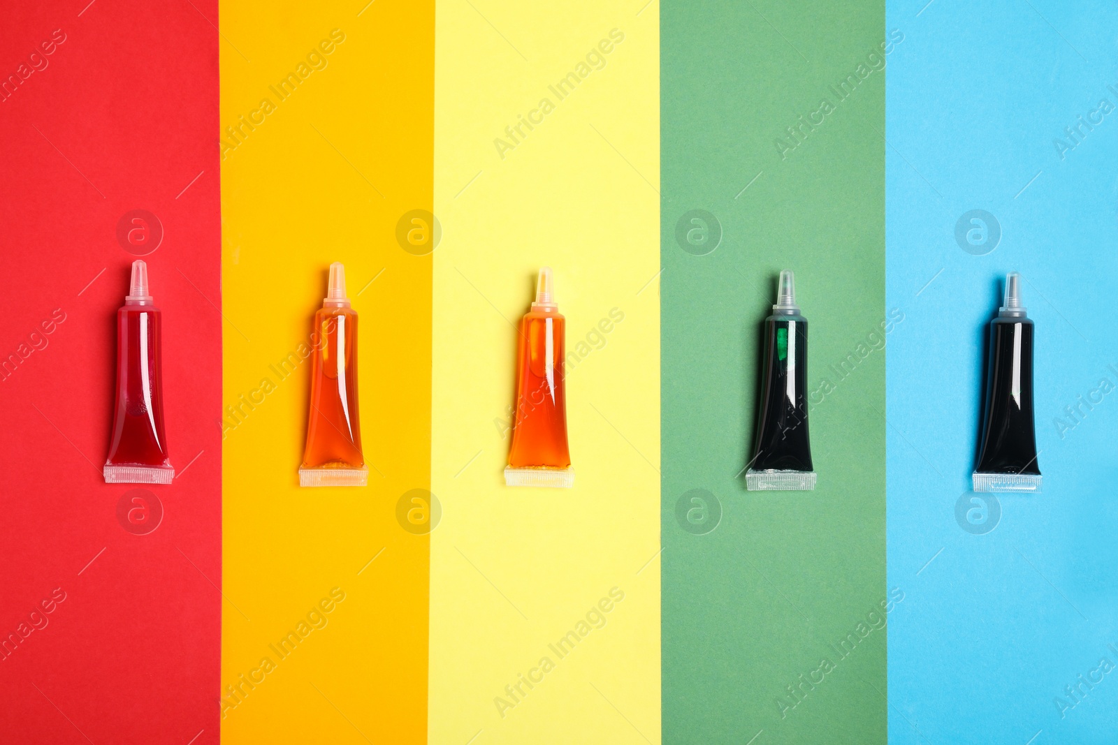 Photo of Tubes with different food coloring on rainbow background, flat lay