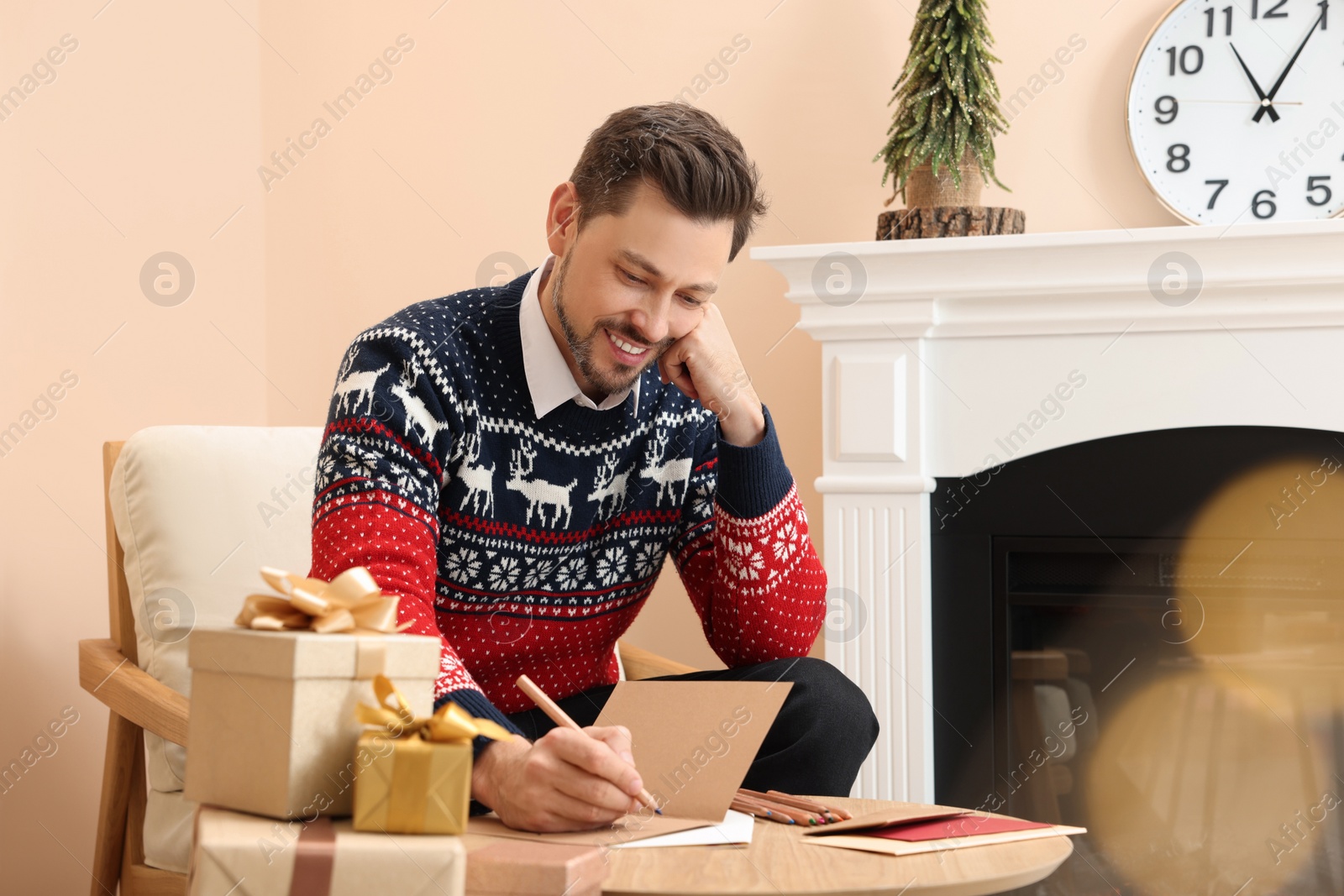 Photo of Happy man writing wishes in Christmas greeting card in living room