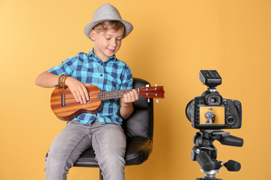 Little music teacher recording guitar lesson on yellow background