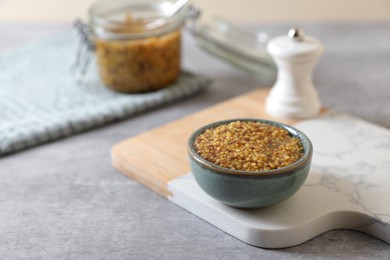 Photo of Wooden board with bowl of delicious whole grain mustard on grey table, space for text