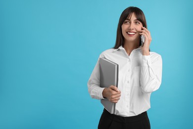 Photo of Happy secretary with folder talking on smartphone against light blue background. Space for text