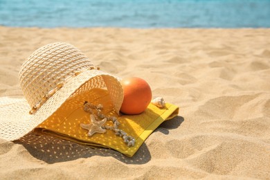 Straw hat, towel and orange on sandy beach. Space for text