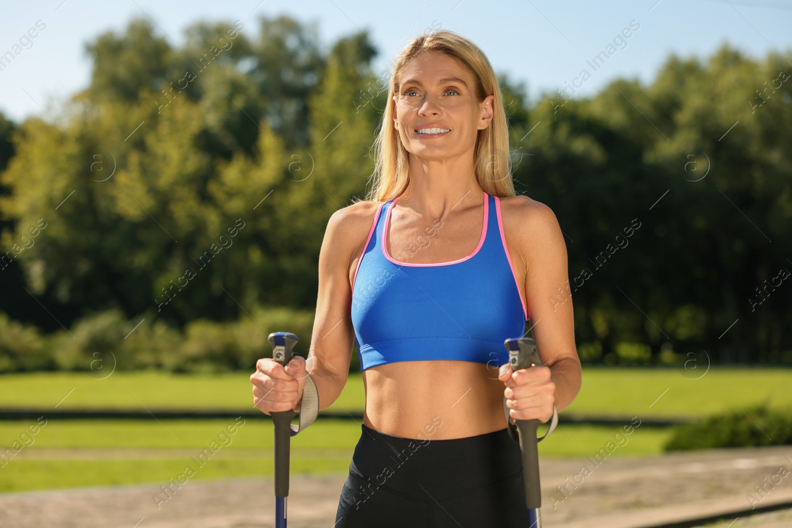 Photo of Happy woman practicing Nordic walking with poles in park on sunny day