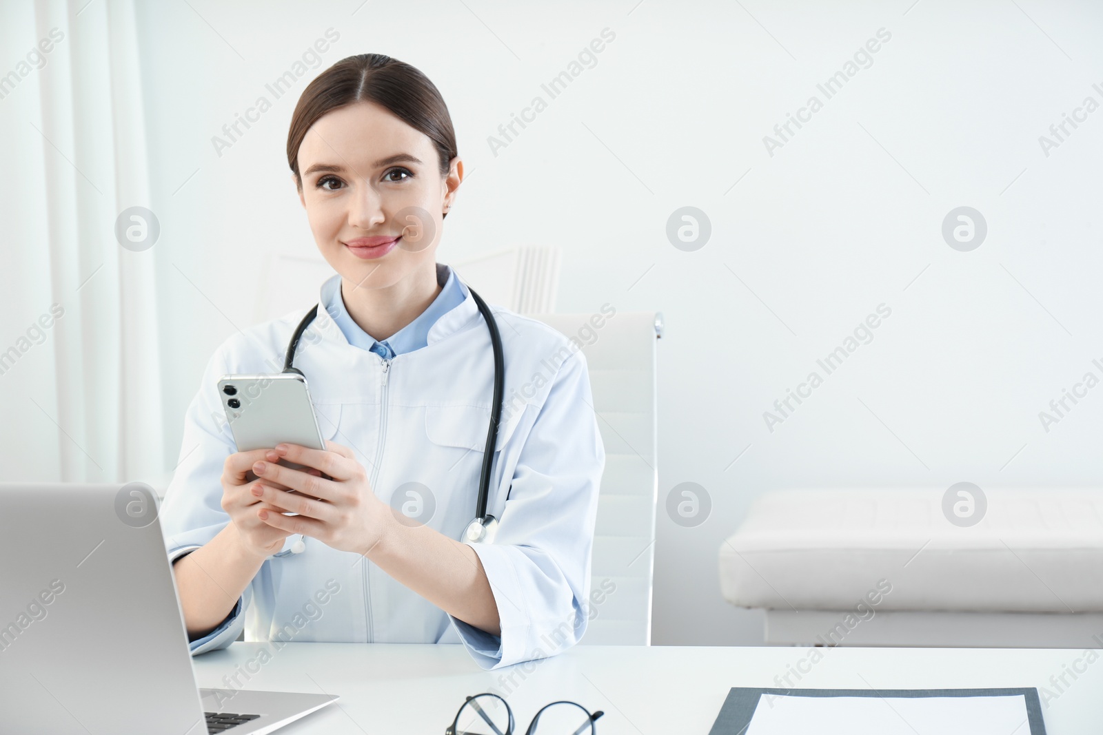 Photo of Young female doctor with smartphone at table in office