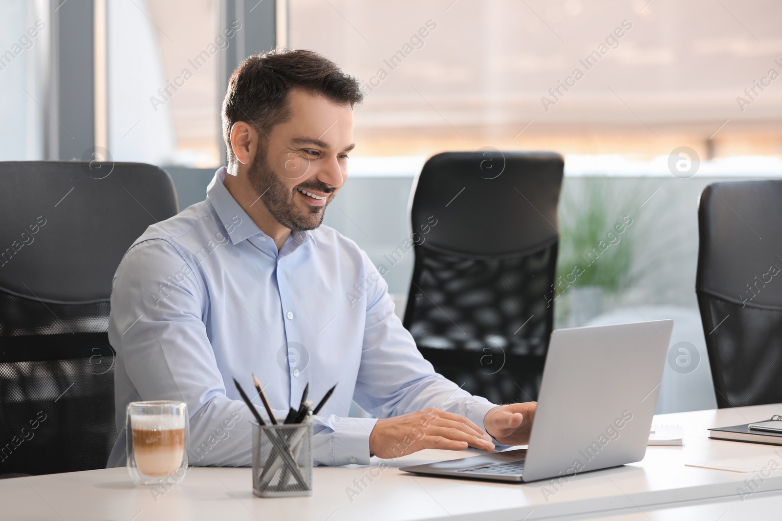 Photo of Happy man using modern laptop at white desk in office