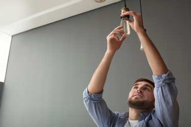 Photo of Man changing lamp light bulb indoors. Space for text