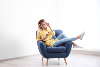 Young woman listening to music in armchair at home. Space for text