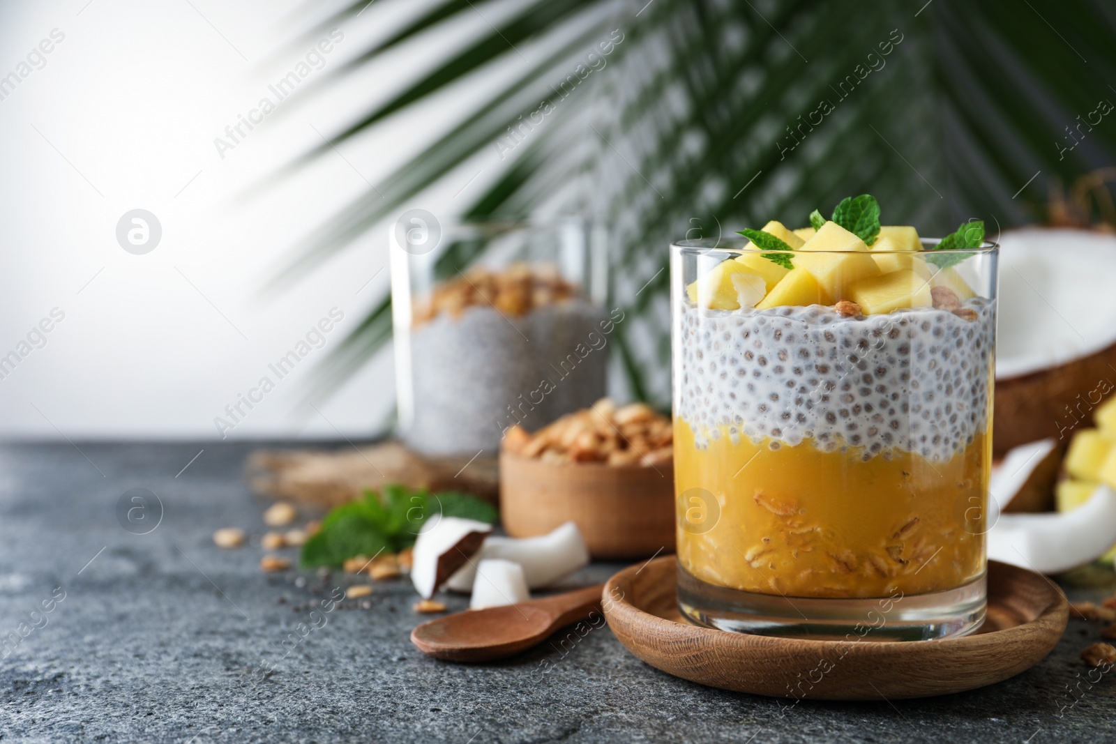 Photo of Delicious chia pudding with mango, mint and granola on grey table, space for text