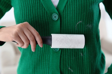 Woman removing hair from green knitted jacket with lint roller on light background, closeup