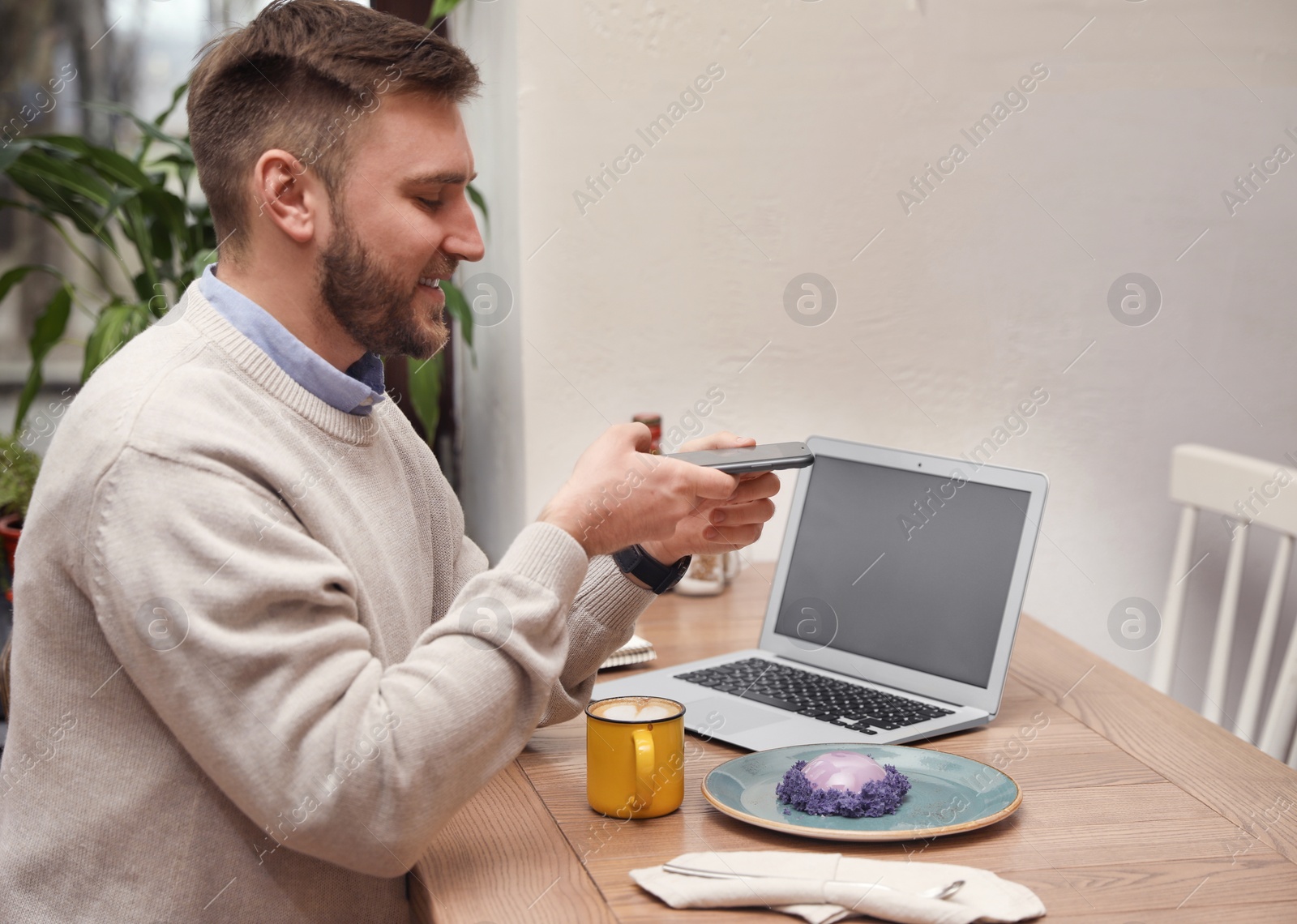 Photo of Male blogger taking photo of dessert and coffee at table in cafe