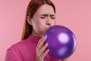 Woman inflating purple balloon on pink background