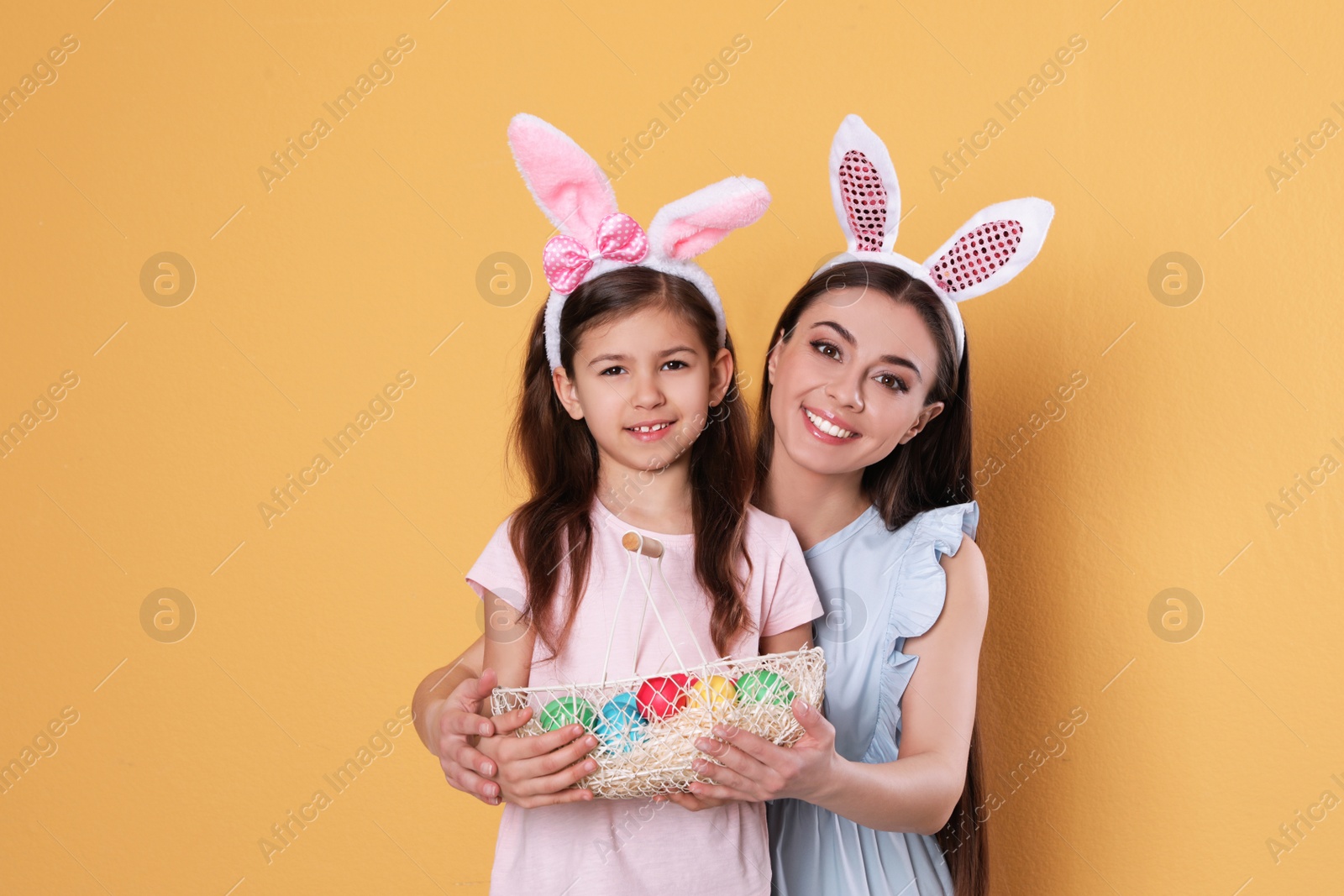 Photo of Mother and daughter in bunny ears headbands with Easter eggs on color background