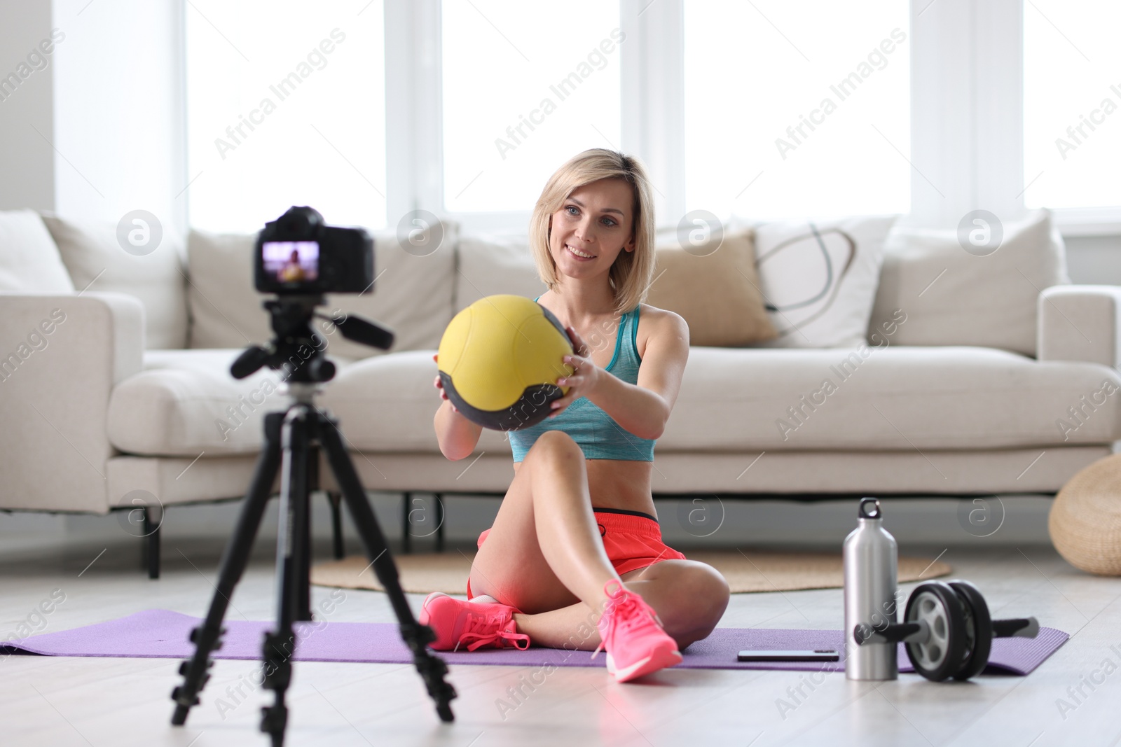 Photo of Smiling sports blogger holding medicine ball while recording fitness lesson with camera at home