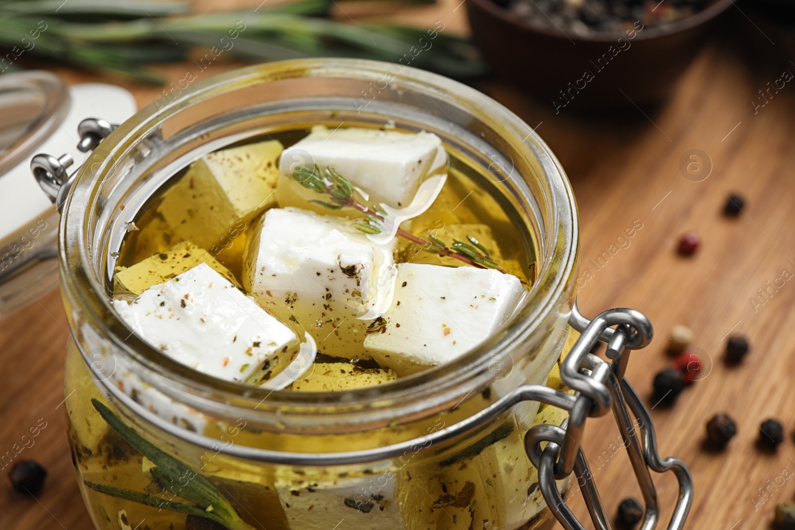 Photo of Jar with feta cheese marinated in oil on wooden table, closeup. Pickled food