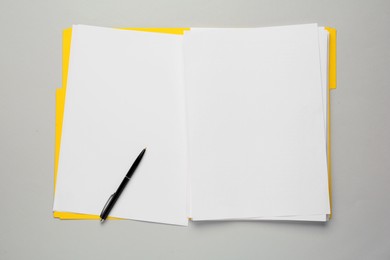 Photo of Yellow file with blank sheets of paper and pen on light grey background, top view. Space for design