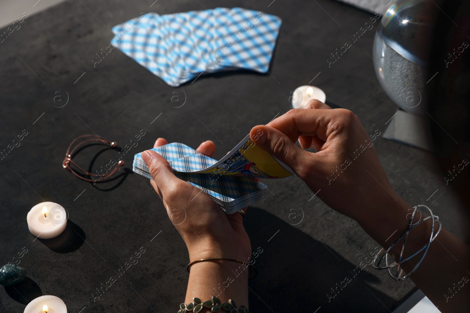 Photo of Fortune teller with deck of tarot cards at grey table, closeup