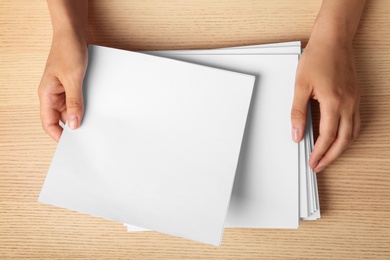 Woman holding blank paper sheets for brochure at wooden table, top view. Mock up