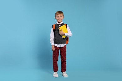 Photo of Happy schoolboy with backpack and books on light blue background