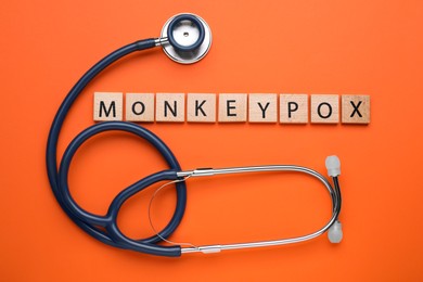 Word Monkeypox made of wooden squares and stethoscope on orange background, flat lay