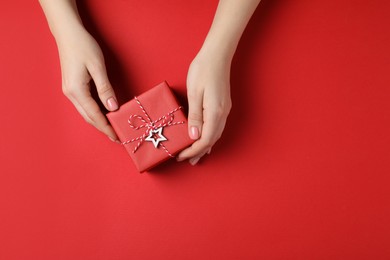 Photo of Woman with beautifully wrapped Christmas gift box on red background, top view. Space for text