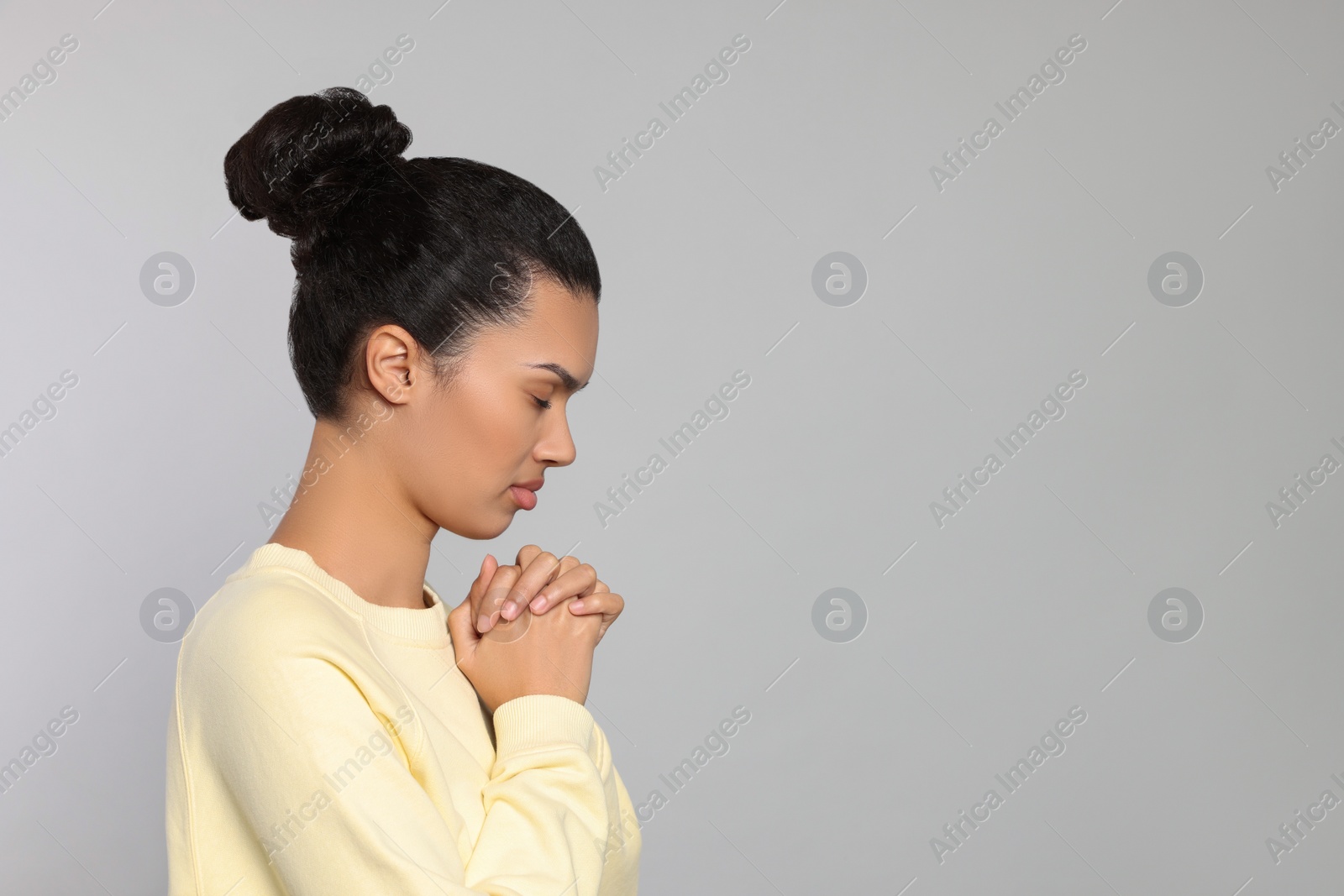 Photo of African American woman with clasped hands praying to God on light grey background. Space for text