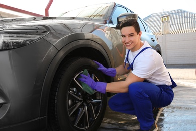 Male worker cleaning automobile with rag at car wash