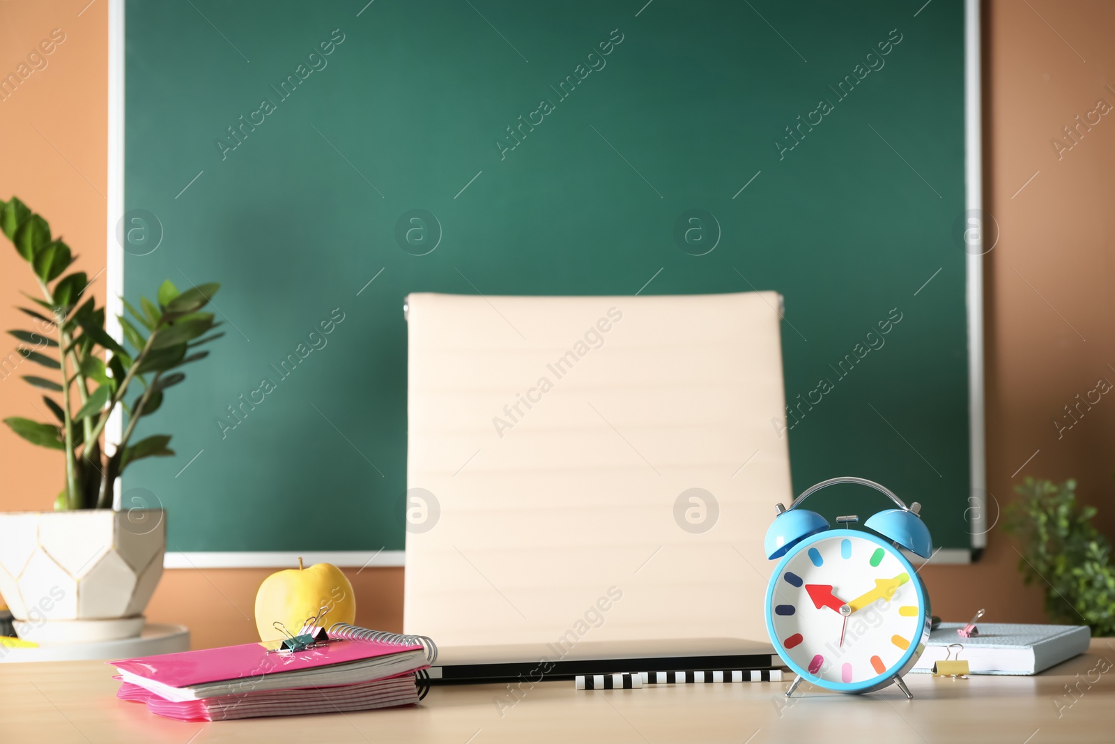 Photo of Notebooks, apple and alarm clock on table in classroom. Teacher day celebration