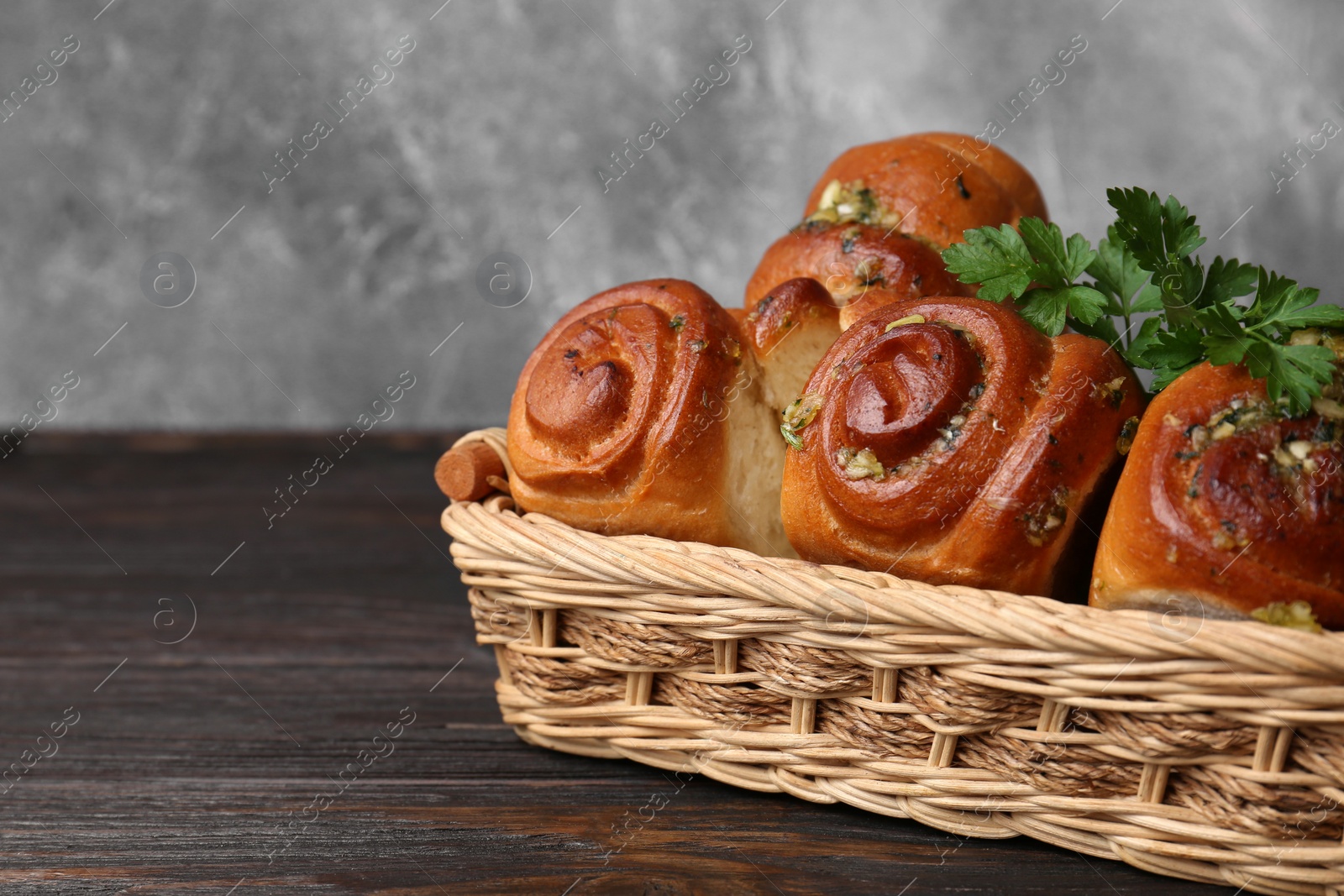 Photo of Delicious pampushky (buns with garlic) in wicker basket on wooden table, space for text