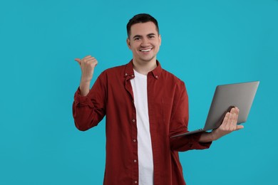 Photo of Special promotion. Happy young man with laptop pointing at something on light blue background, space for text