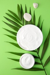 Photo of Jars of cream, leaf and stones on light green background, flat lay