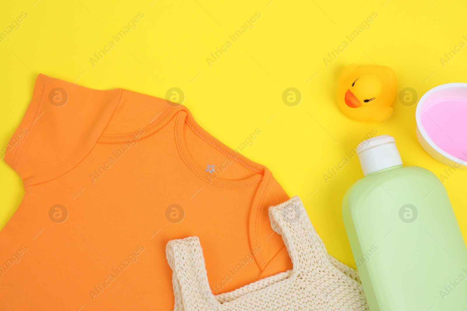 Photo of Laundry detergents, baby clothes and rubber duck on yellow background, flat lay