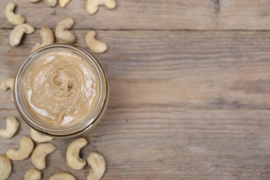 Photo of Tasty cashew nut paste in jar on wooden table, top view. Space for text