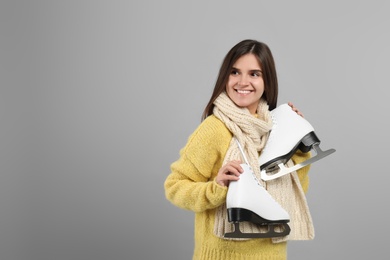 Happy woman with ice skates on grey background. Space for text