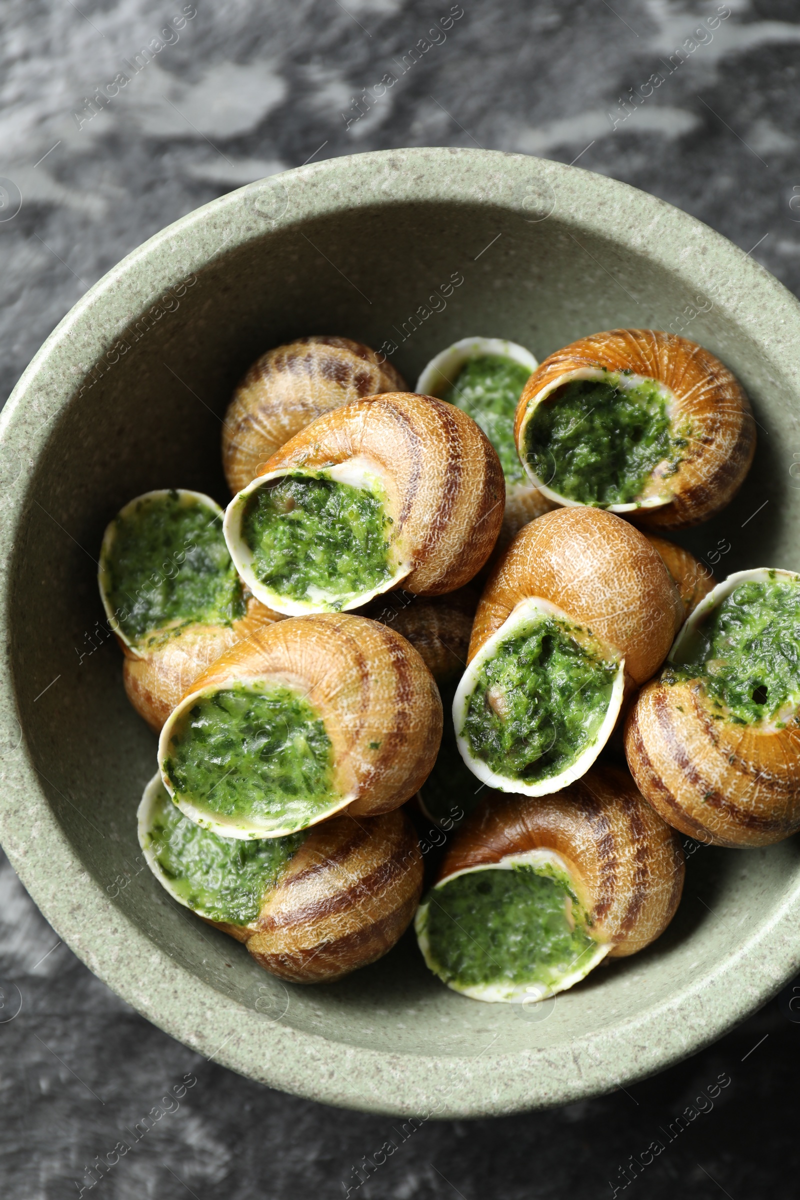 Photo of Delicious cooked snails in bowl on dark table, top view