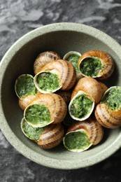 Delicious cooked snails in bowl on dark table, top view